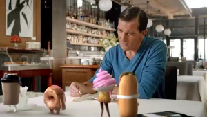 Antonio Banderas reaches across a restaurant table to touch a pink animated doughnut in an Extra commercial.